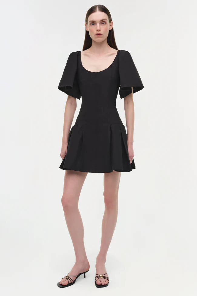 Model wearing a black cotton faille mini dress with an architectural silhouette, including a fitted, seamed bodice, statement puff sleeves, and an easy flared skirt