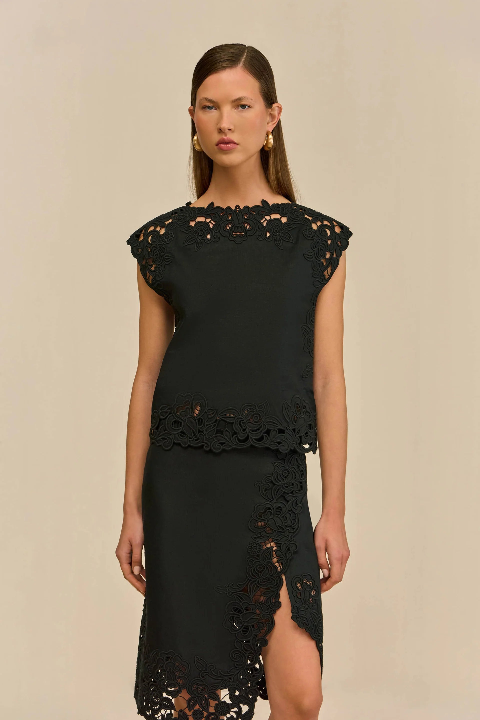 Model wearing a white Cult Gaia Destry Top in breathable linen, with embroidered cutouts on the high neckline, cap sleeves, and hem, styled with a straight, slightly relaxed fit.