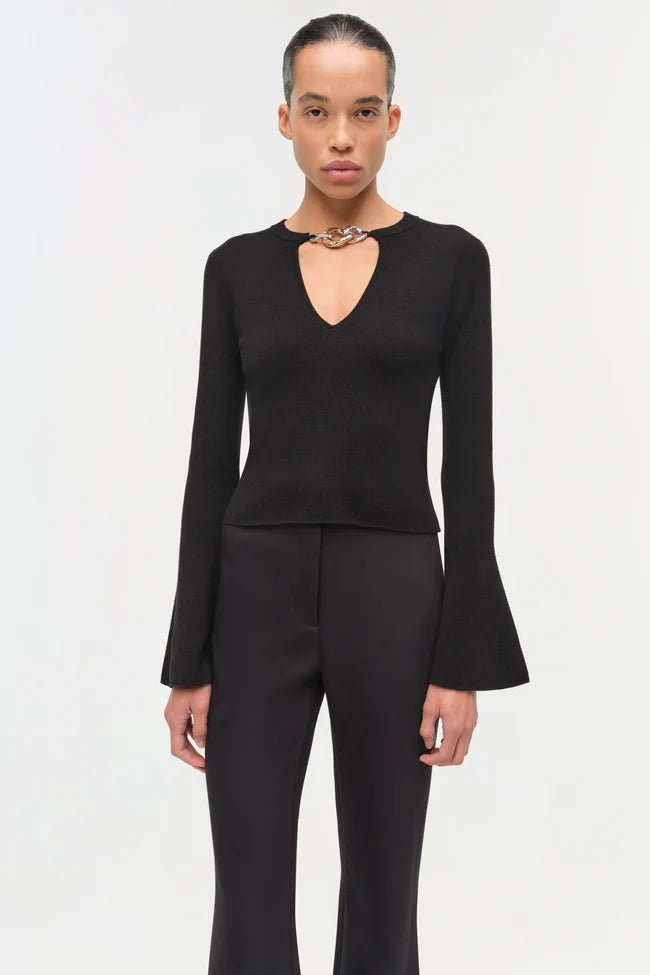 Model wearing a black superfine merino wool top with a chain-link keyhole neckline and subtly flared long sleeves, creating a sleek, elongating silhouette.