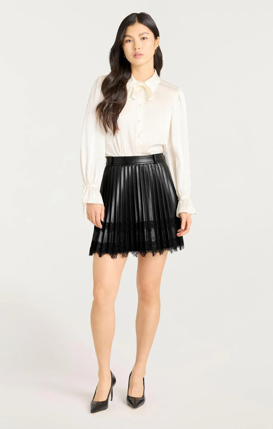 Model wearing the Cinq à Sept Laney Skirt, a mini-length vegan leather skirt with pleated design, lace detailing, and a concealed side zipper closure.