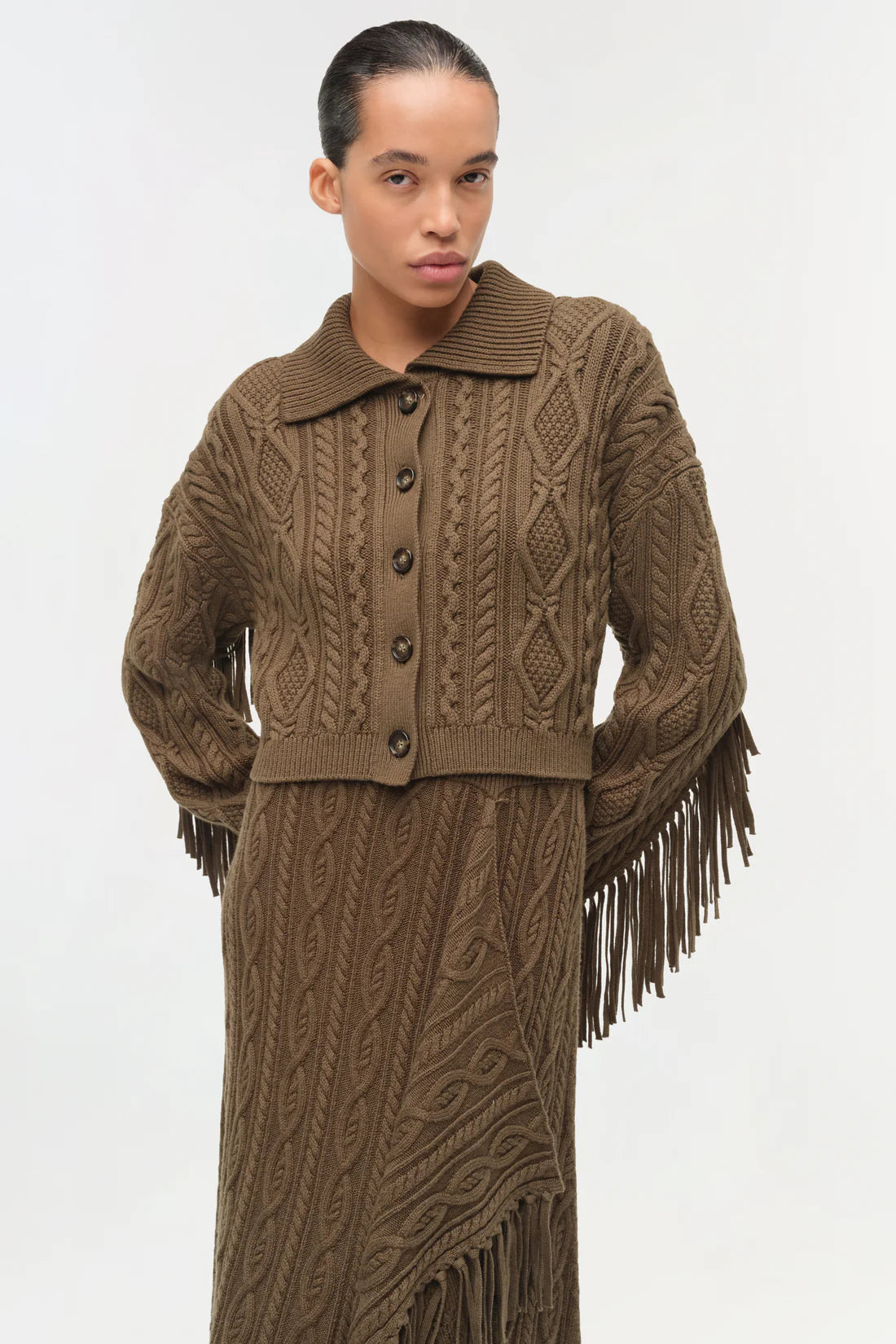 Simkhai Virginia Wool Fringe Cardigan in pine green featuring a cropped cable knit design, pointed collar, button-front closure, and fringe detailing along the back and sleeves