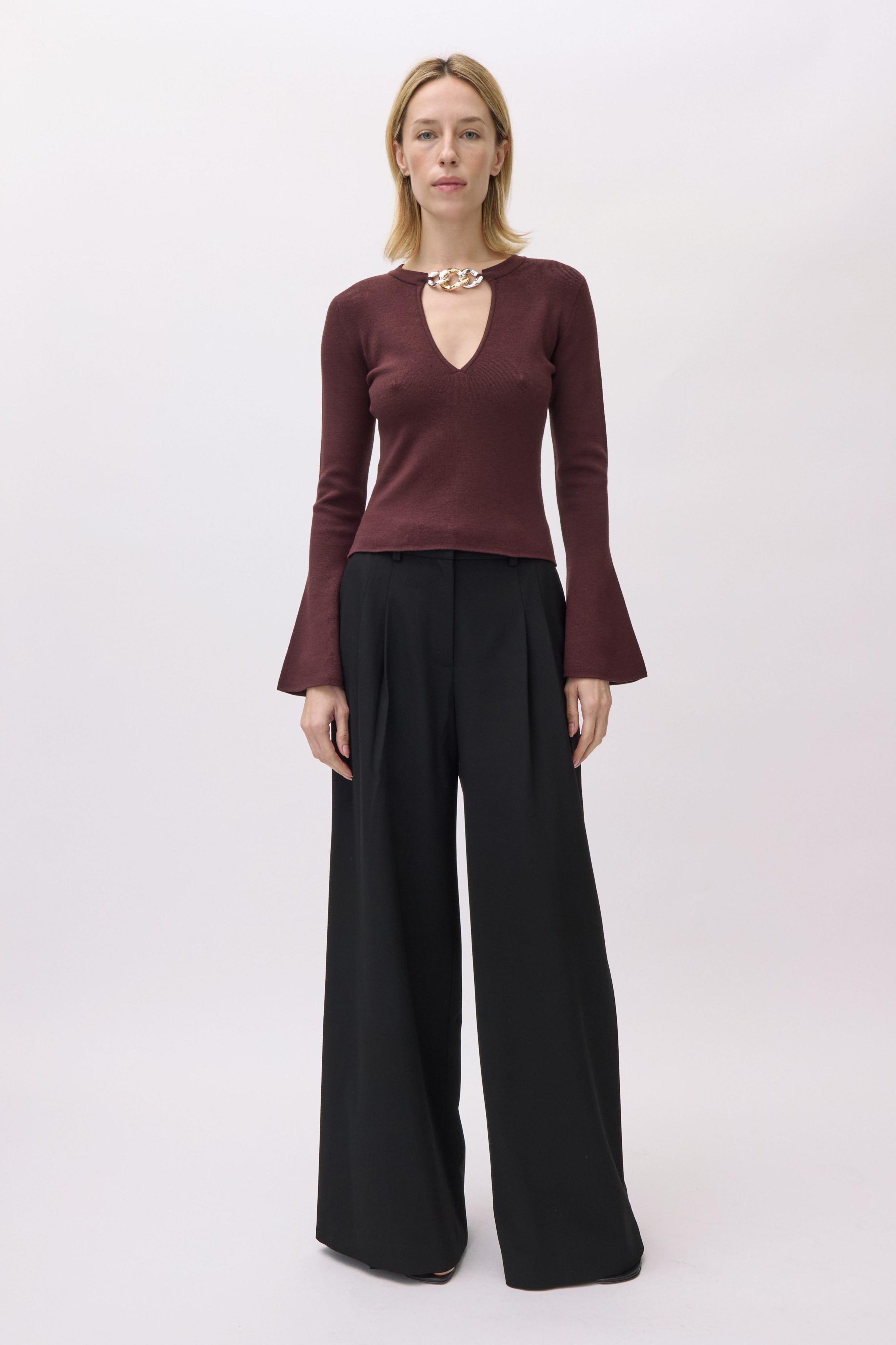 Woman wearing a burgundy long-sleeve top and black wide-leg pants on a white background